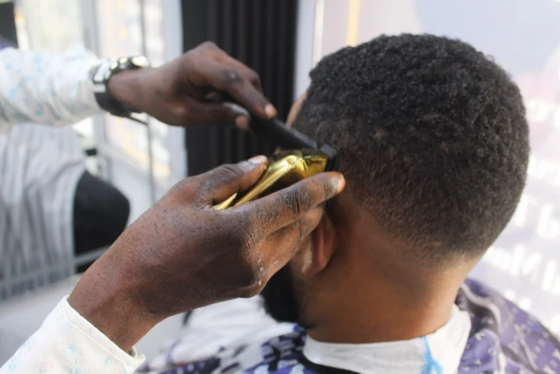 Barber fading a client's hair with gold clippers